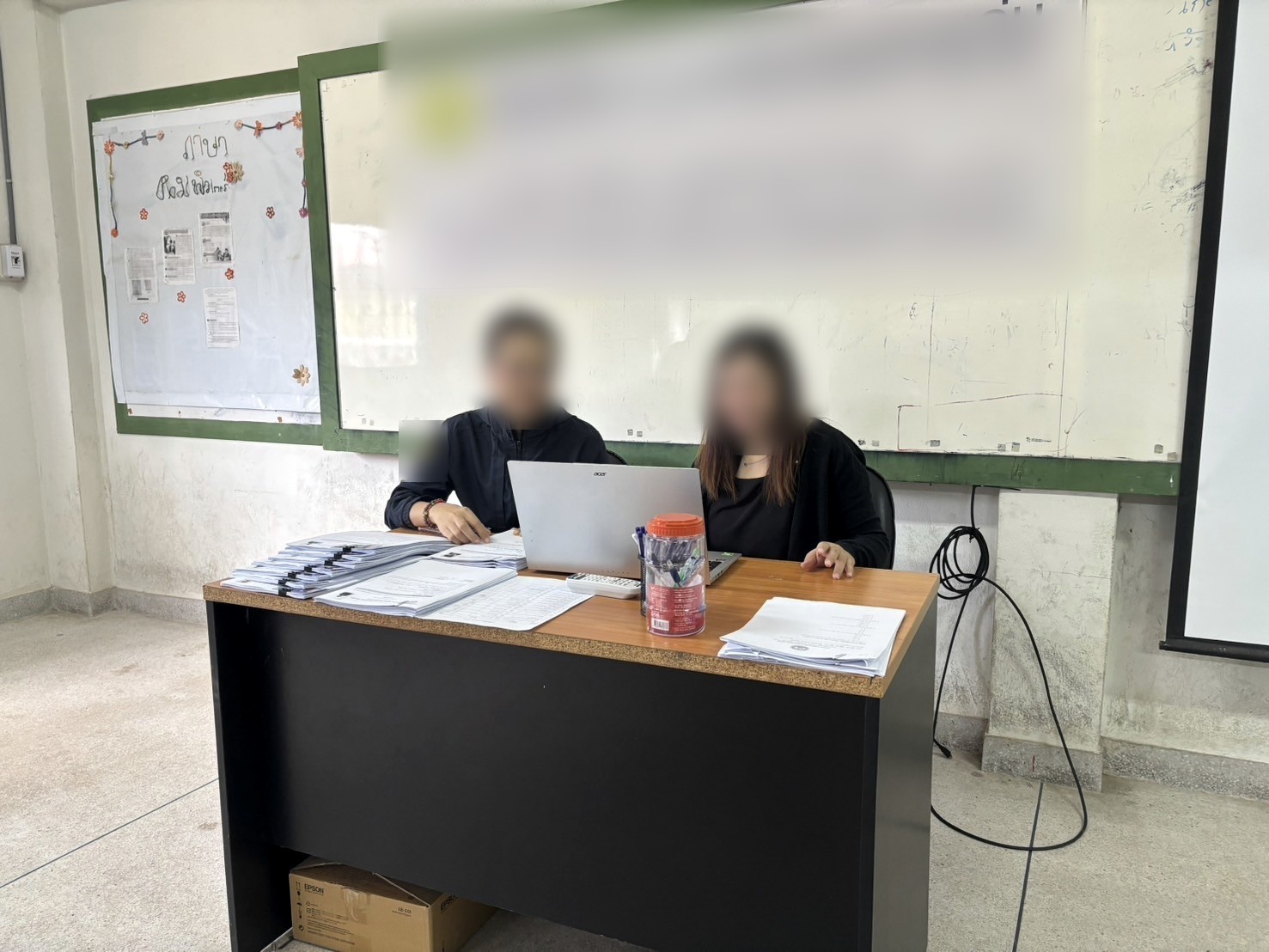 A registration desk with documents and a laptop; faces and signage obscured